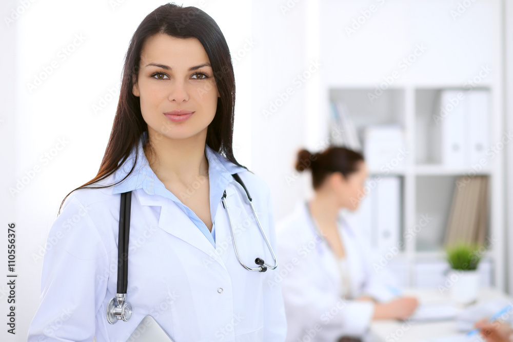 Brunette female doctor on the background of colleagues talking to each other in hospital Brunette female doctor on the background of colleagues talking to each other in hospital