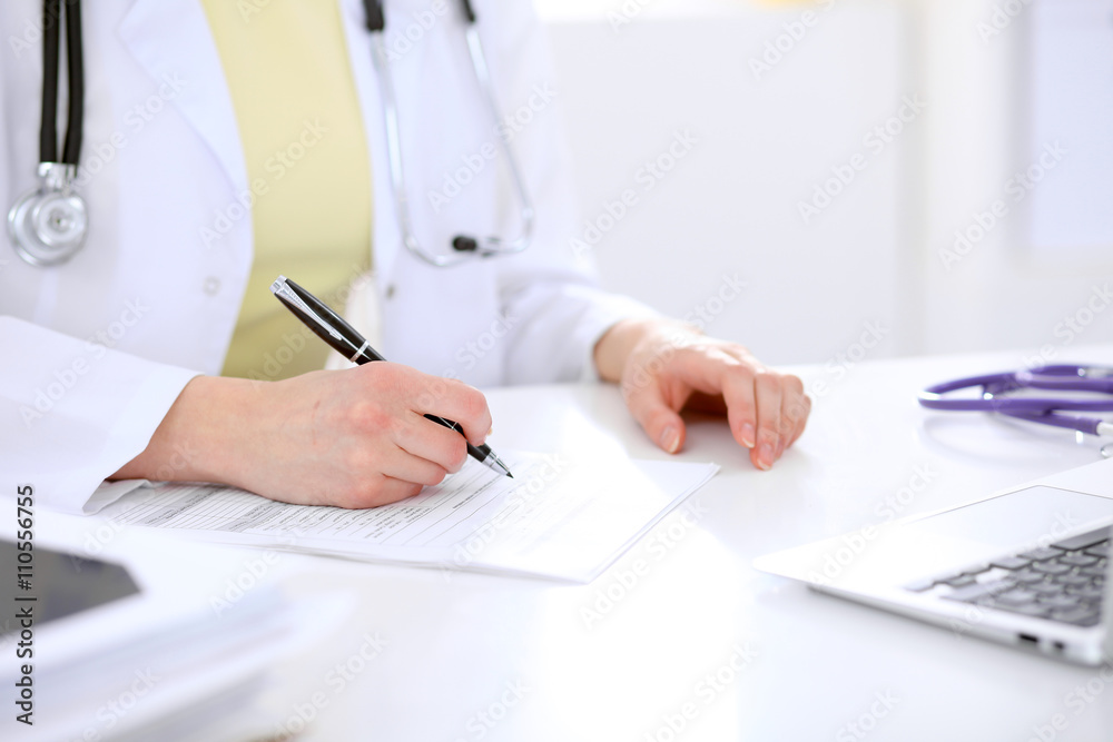 Close-up of a female doctor filling out application form , sitting at the table in the hospital Close-up of a female doctor filling out application form , sitting at the table in the hospital