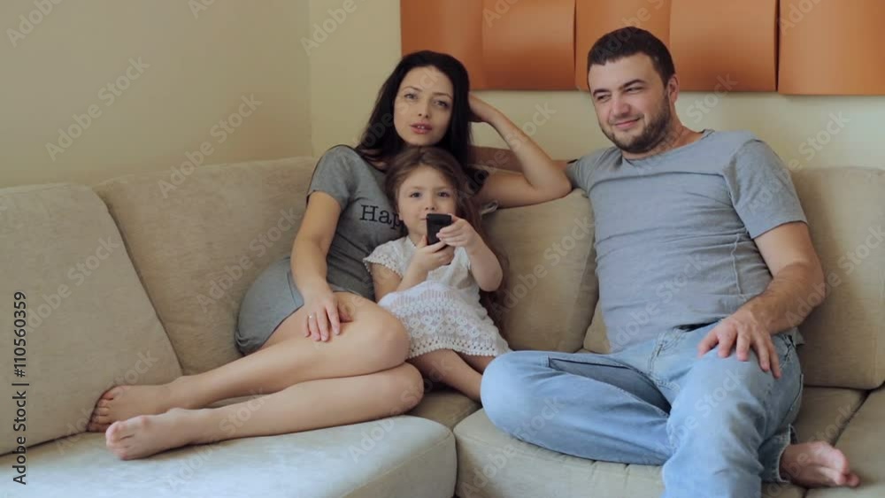 Young family watching television sitting on sofa Young family watching television sitting on sofa