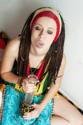 A young girl, dreadlock Rasta and Rasta hat, smokes drugs throug photo