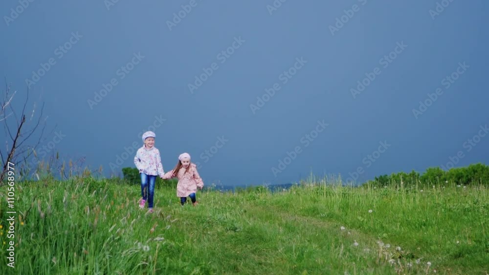 Two little girls running along a country road. Against the background of a stormy sky and approaching rain Two little girls running along a country road. Against the background of a stormy sky and approaching rain