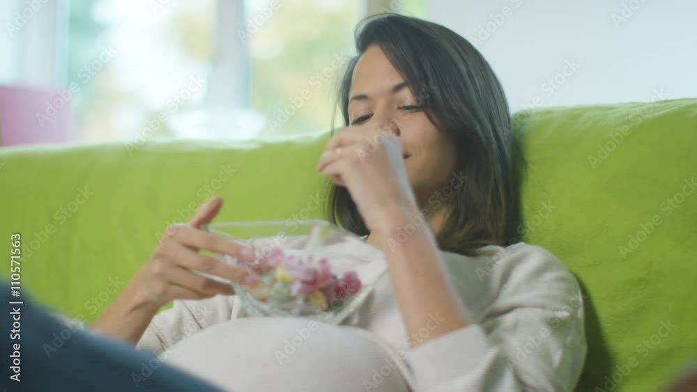 Pregnant woman relaxing at home, woman rests bowl of sweets on her baby bump Pregnant woman relaxing at home, woman rests bowl of sweets on her baby bump