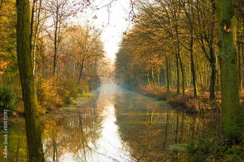 Canal in a autumn colored forest with trees reflecting on the water