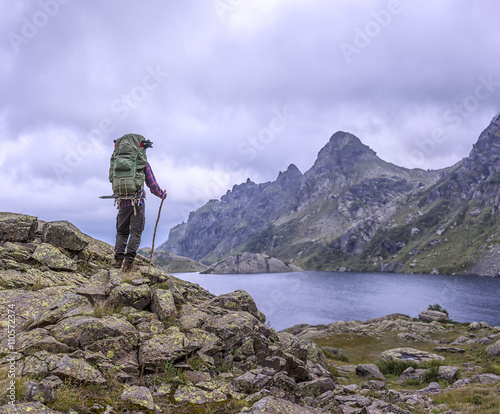 man with a backpack standing on vintage background of high mountains drowning in clouds and clear lake