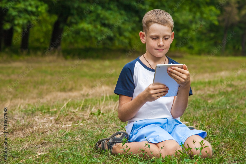 Cute young caucasian kid working with tablet in park. Cute young caucasian kid working with tablet in park.