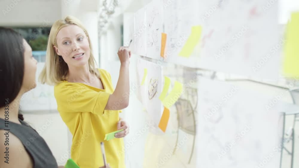 Female creative design team brainstorming for ideas with sticky notes Female creative design team brainstorming for ideas with sticky notes