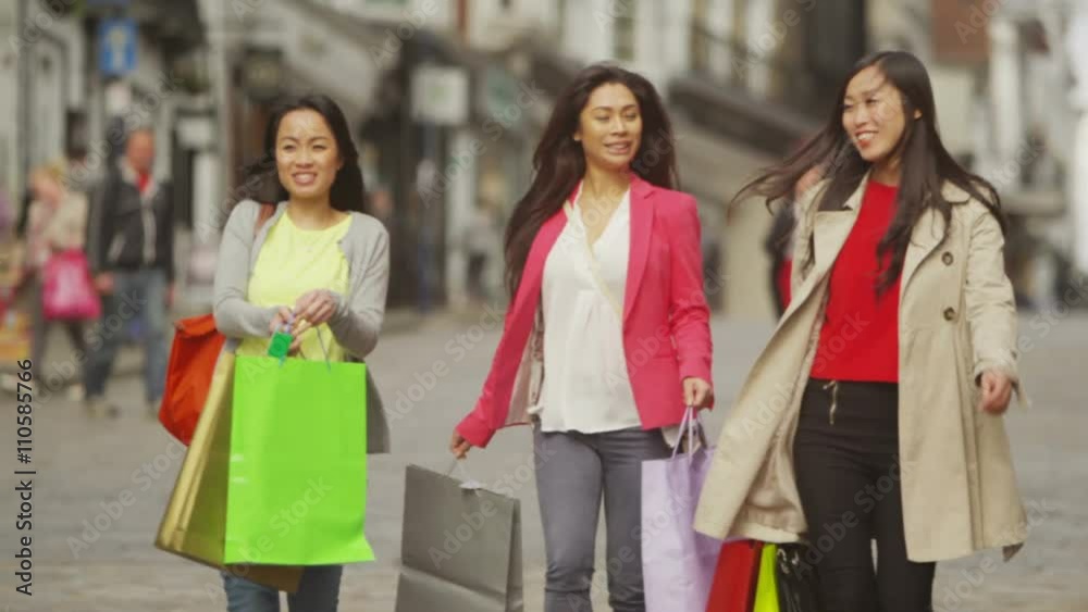 Portrait of attractive Asian female friends walking with colourful bags in busy Portrait of attractive Asian female friends walking with colourful bags in busy