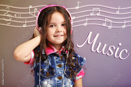 Beautiful little girl with headphones listening to music on color background