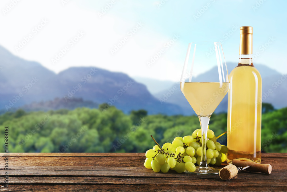 Still life with white wine and bunch of grapes on nature background