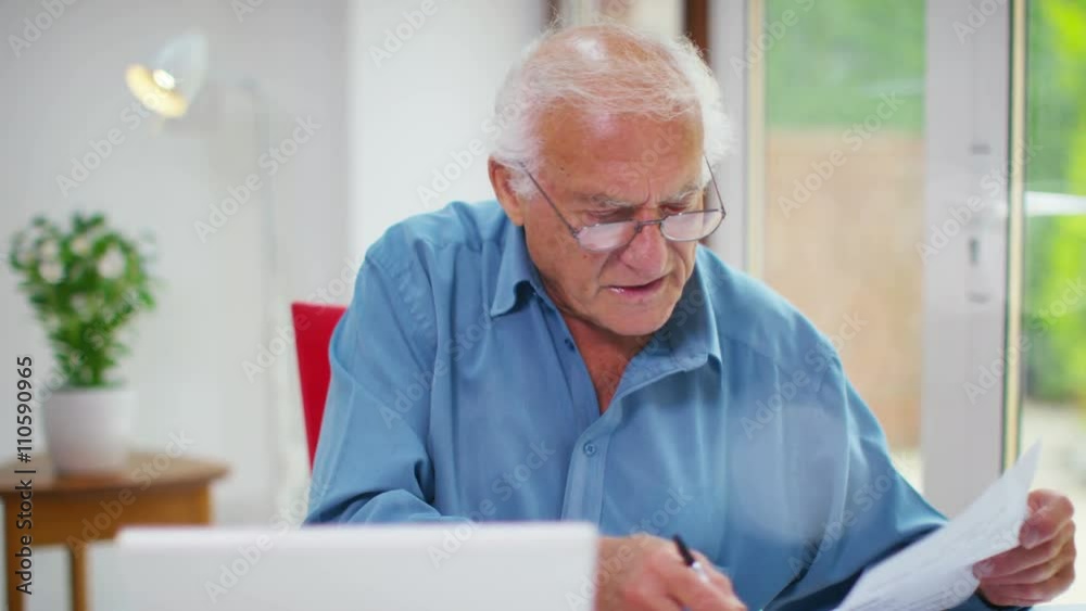  Frustrated senior man working on a laptop computer & looking at paperwork. Shot on RED Epic.