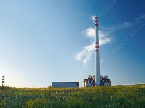 Waste incinerator in the evening sunlight, standing on a green meadow under blue sky.