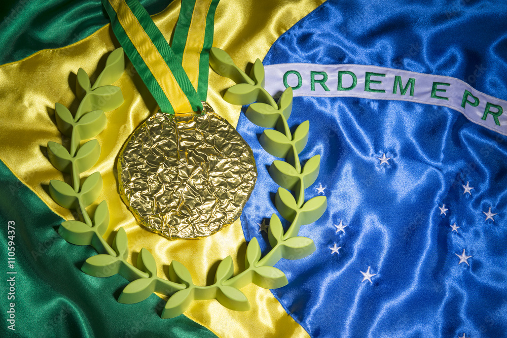 Large gold medal surrounded by laurel wreath resting on shiny Brazil flag background with studio lighting