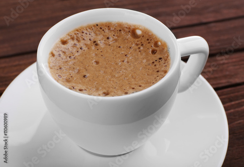 Cup of coffee with brown foam on wooden background, close up