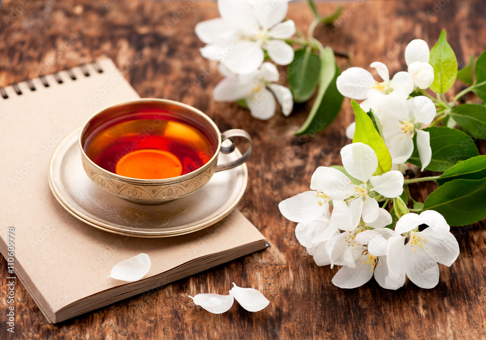 Tea cup, notebook and white spring flowers on a wooden table Tea cup, notebook and white spring flowers on a wooden table