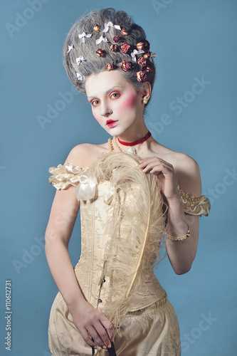 Baroque Style - beautiful young woman with barocco hairstyle posing over blue background in elegant light corset with lace. Renaissance. Rococo. Fashion. photo