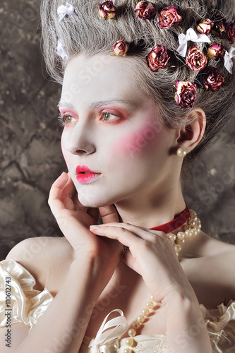 Baroque Style - beautiful young woman with barocco hairstyle posing over vintage grey background in elegant light corset with lace. Renaissance. Rococo. Fashion.