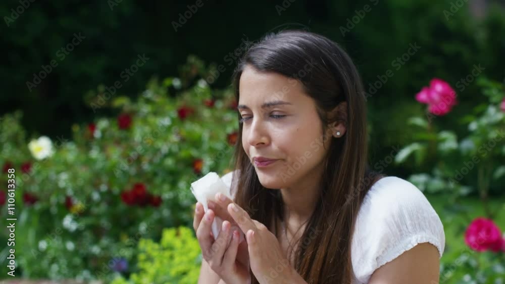 Woman with hay fever sneezes into a tissue as she sits in her garden Woman with hay fever sneezes into a tissue as she sits in her garden