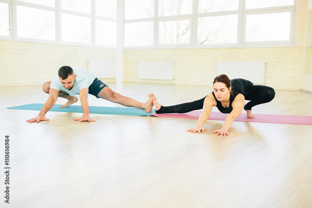 Fototapeta premium Atractive yoga couple , man and woman, practice exercises in a training hall background. Yoga concept.