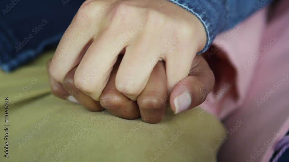 Close up on hands of young mixed ethnicity couple holding hands tightly Close up on hands of young mixed ethnicity couple holding hands tightly