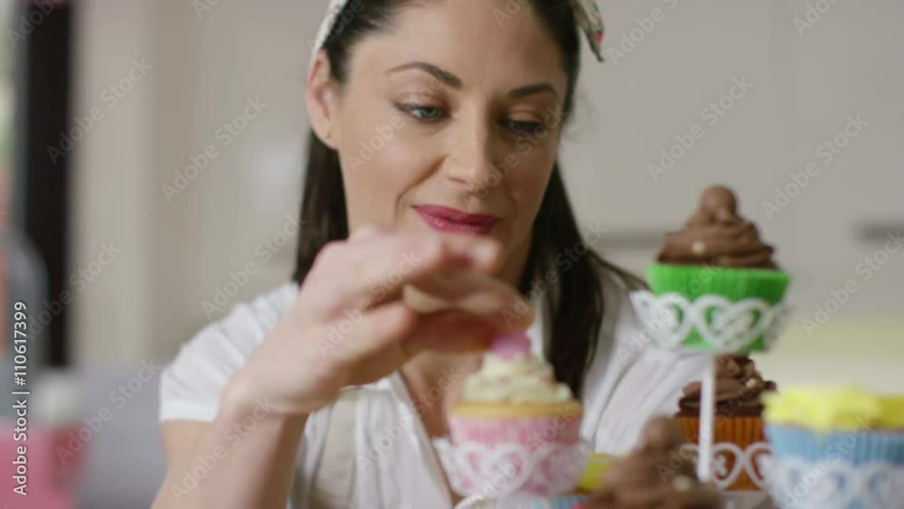 Smiling woman with bakery business putting finishing touches onto cupcakes Smiling woman with bakery business putting finishing touches onto cupcakes