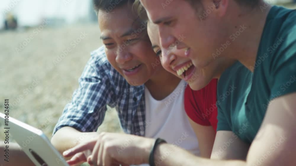 Happy mixed ethnicity group of friends using computer tablet at the beach Happy mixed ethnicity group of friends using computer tablet at the beach