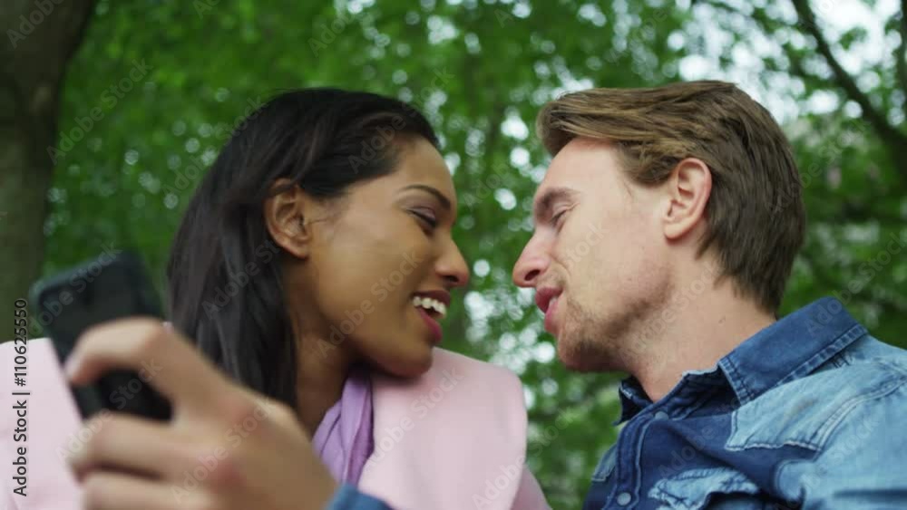 Romantic mixed ethnicity couple pose for a selfie in the park Romantic mixed ethnicity couple pose for a selfie in the park