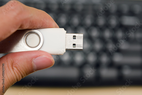 Hand hold blank USB thumb drive with keyboard in the background