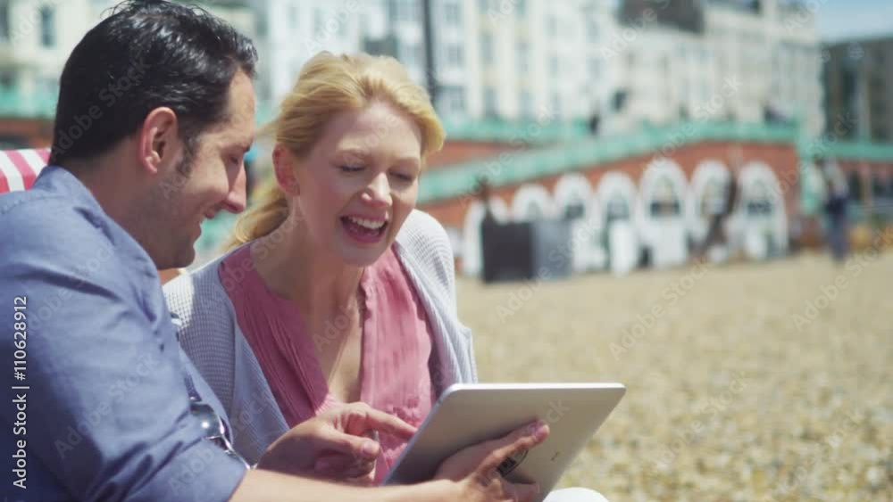 Couple on beach with computer tablet laughing at what they see on the screen Couple on beach with computer tablet laughing at what they see on the screen