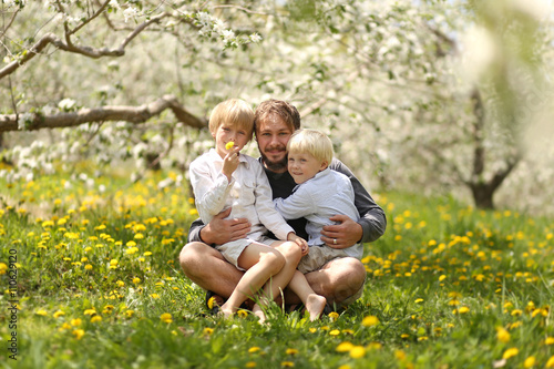 Portrait of Happy Father and Two Young Children Hugging on  a Spring Day in a flowering Apple Orchard