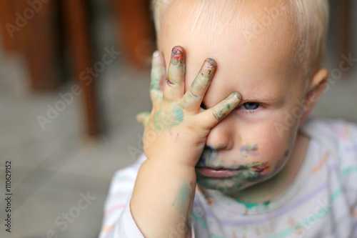 One Year old Baby Girl Covering her messy painted face with her little hand photo