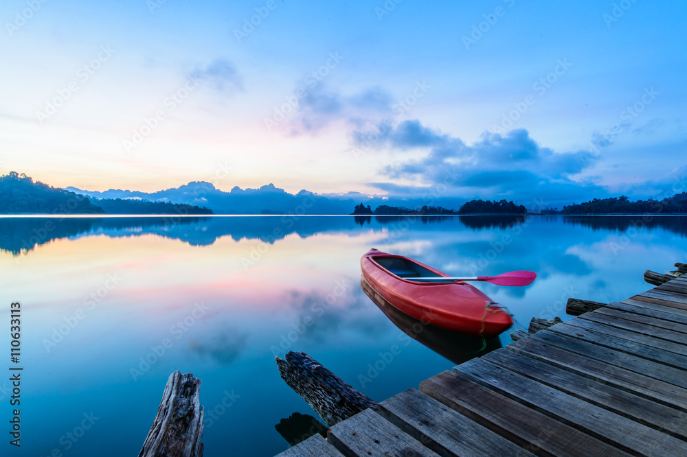 Fototapeta Canoe floating on the calm water under amazing sunrise