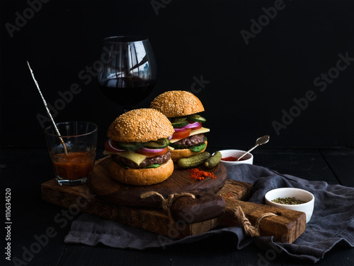 Fresh beef burgers on rustic wooden boards with glass of wine and tomato sauce, black background.