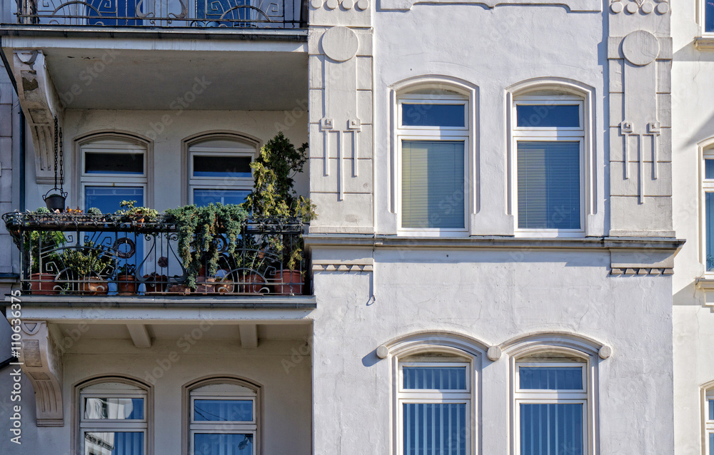 wunderschöne Fassade eines Altbaus mit filigranen Stuckarbeiten und kleinem Balkon mit Balkonpflanzen 