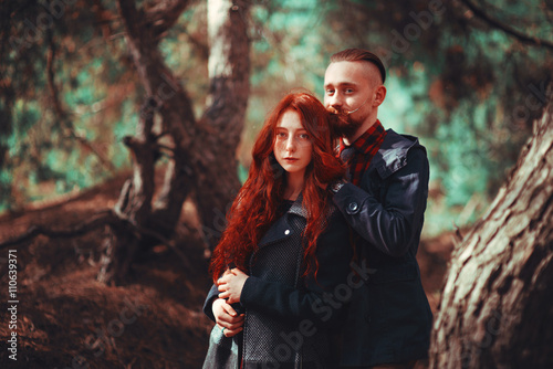 The red-haired guy with a beard and curly red-haired girl on the background of fabulous scenery of nature. Beautiful loving couple on a walk in the woods. © nalliens