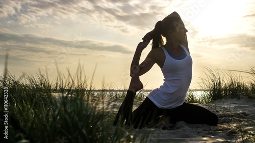 Young woman in a mermaid yoga pose on a sandy beach at sunset