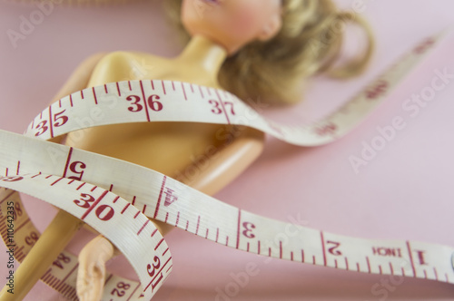 closeup measuring tape with women plastic doll on pink background
