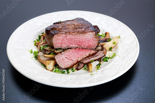 Tasty Beef Mignon steak with mushrooms and herbs on plate.