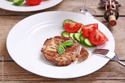 Roasted beef fillet and fresh vegetables on plate, on wooden background