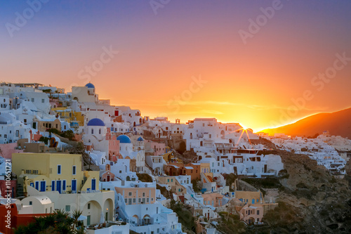 Old Town of Oia on the island Santorini, white houses and church with blue domes at sunrise, Greece © Kavalenkava