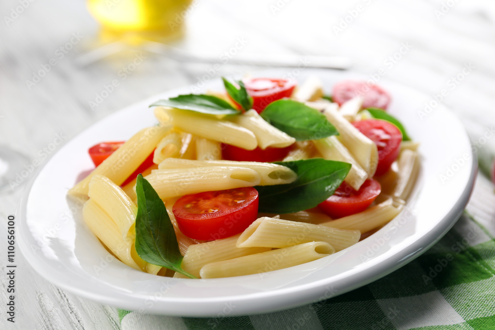 Plate of pasta with cherry tomatoes and basil leaves on table closeup Plate of pasta with cherry tomatoes and basil leaves on table closeup