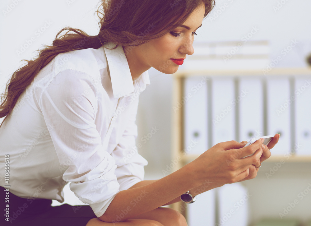 Businesswoman sending message with smartphone sitting in the office