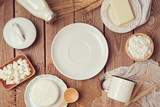 Milk, cheese and butter around empty white plate on wooden background. Healthy eating concept. View from above. Flat lay.