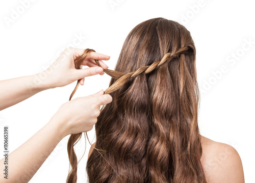 Hands hairdresser braided lock of the girl with long hair isolated on white .