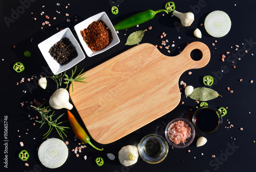 Food background. Empty cutting board and pepper, bay leaf, rosemary, onions, Himalayan salt, olive oil, soy sauce on a black background. The template for displaying products