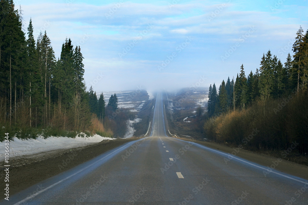 Fototapeta premium A hilly winter road with a forest around and the road going up and down 