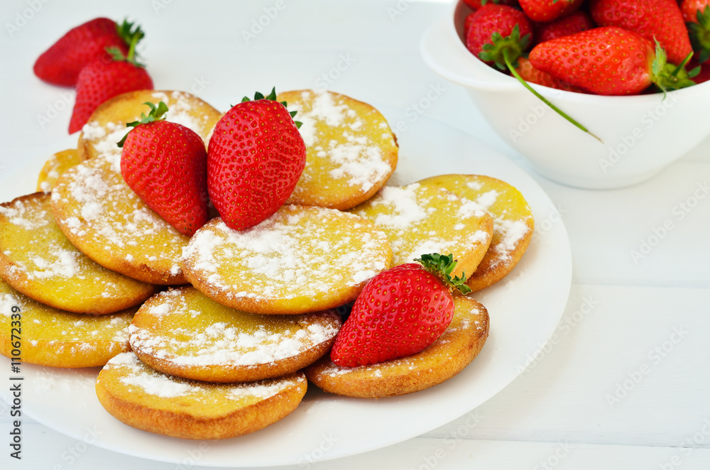 Pancakes with powdered sugar decorated with whole strawberries on a white plate on a white table