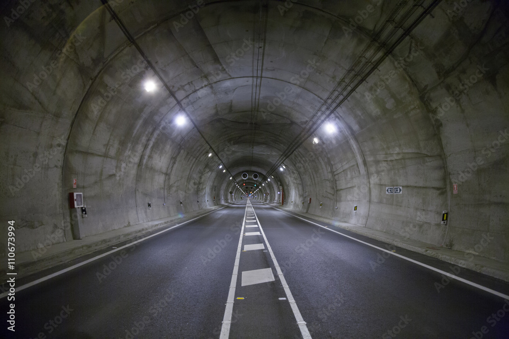 Fototapeta premium landscape straight grey lonely road tunnel with two lanes, white painting dividing lines in asphalt and light, in Spain Europe