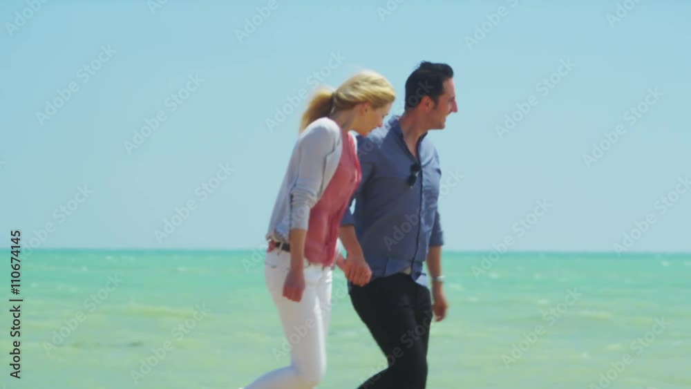 Attractive romantic couple holding hands as they walk along the beach Attractive romantic couple holding hands as they walk along the beach