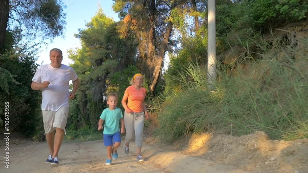 Steadicam slow motion shot of parents and child jogging in the park or forest in sunny day.