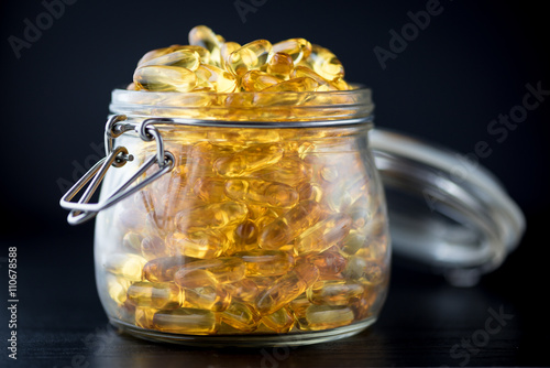 Omega 3-6-9 fish oil yellow softgels on wooden black board into airtight glass jar